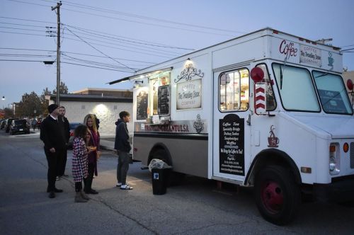 A coffee truck with a menu, people waiting in line, and a dusk sky in the background.