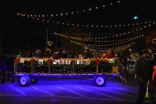 A festive parade float decorated with lights and greenery, surrounded by people enjoying a nighttime celebration.
