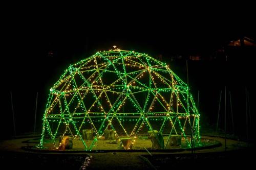 A geodesic dome illuminated with green lights at night, surrounded by a dark landscape.