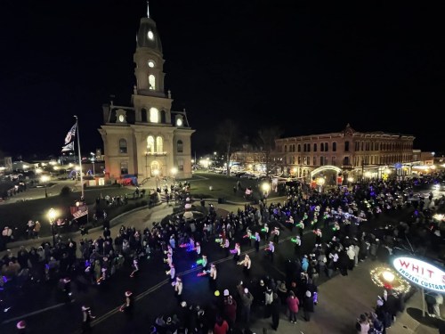A nighttime parade with colorful lights in front of a historic building, bustling with people celebrating.