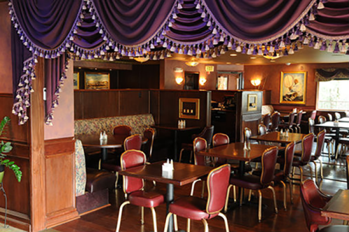 Cozy restaurant interior with purple drapes, wooden accents, and tables set for dining.
