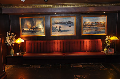 Cozy lounge area with a red upholstered bench, decorative lamps, and three framed landscape paintings on the wall.