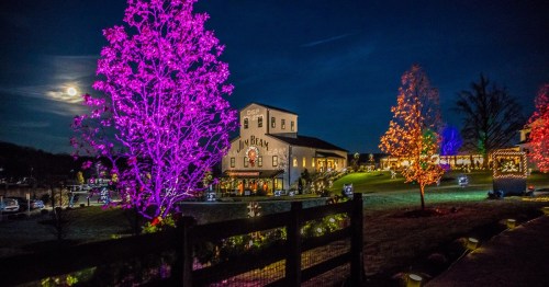 A brightly lit building surrounded by colorful trees at night, with a full moon in the sky.