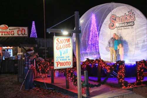 A festive scene featuring a snow globe attraction with families inside, surrounded by holiday lights and decorations.