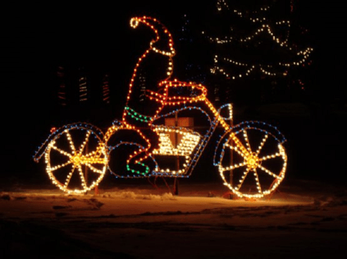 A festive light display featuring a bear in a Santa hat riding a motorcycle, surrounded by colorful holiday lights.