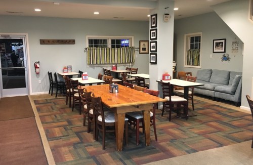 Cozy dining area with wooden tables, chairs, and a couch, featuring a warm color scheme and decorative wall art.