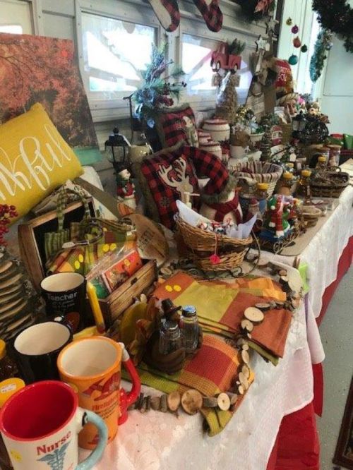 A festive display of handmade crafts, decorations, and seasonal items on a table, featuring mugs, baskets, and colorful textiles.