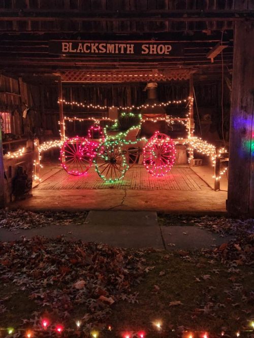 A blacksmith shop decorated with colorful holiday lights, featuring a bicycle made of red and green lights.