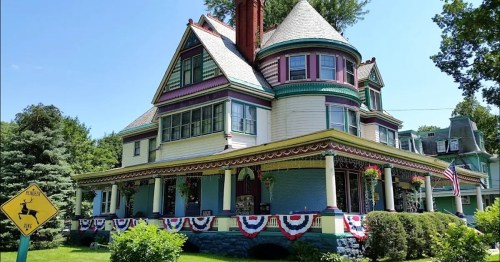 Victorian-style house with colorful trim, a turret, and patriotic bunting adorning the porch and garden.