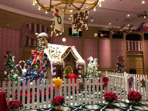 A festive room decorated for Christmas, featuring a gingerbread house, colorful trees, and holiday ornaments.