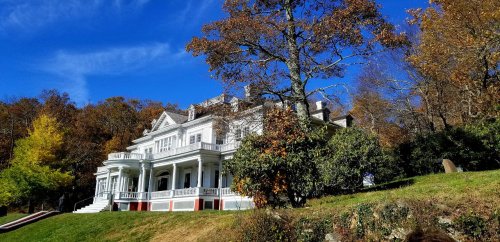 A large white mansion surrounded by colorful autumn trees under a clear blue sky.