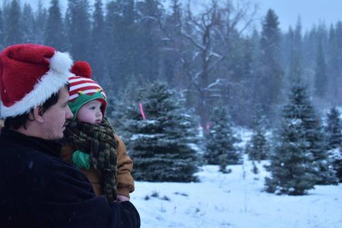 A man in a Santa hat holds a child in winter attire, surrounded by snow-covered trees.