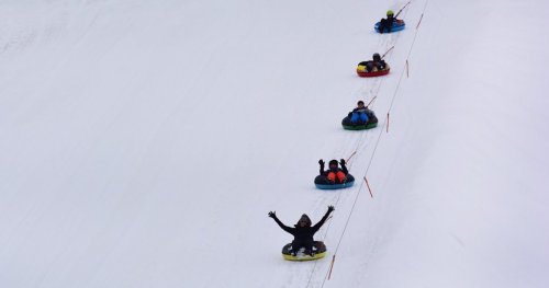 A group of people sledding down a snowy hill on colorful tubes, with one person joyfully raising their arms.