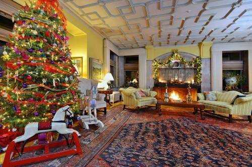 Cozy living room decorated for Christmas, featuring a large tree, fireplace, and festive furnishings.