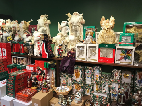 A festive display of various Christmas decorations, including Santa figures, ornaments, and gift wrap, on shelves.