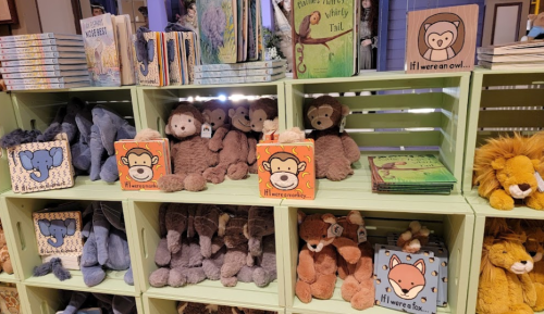 A display of plush animals and children's books on shelves, featuring bears, monkeys, and a fox.