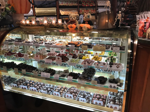 A display case filled with various chocolates and candies, decorated with Halloween-themed plush toys and candles.