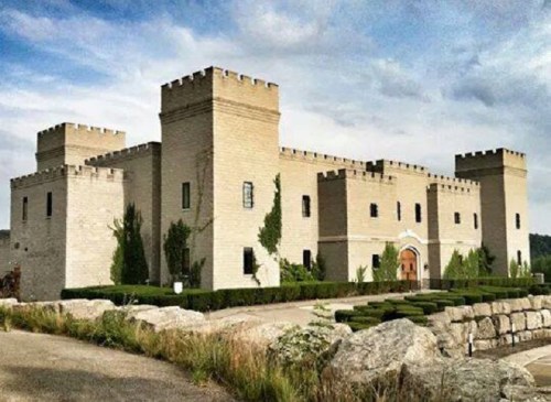 A large, light-colored castle with towers, surrounded by greenery and a stone pathway in the foreground.
