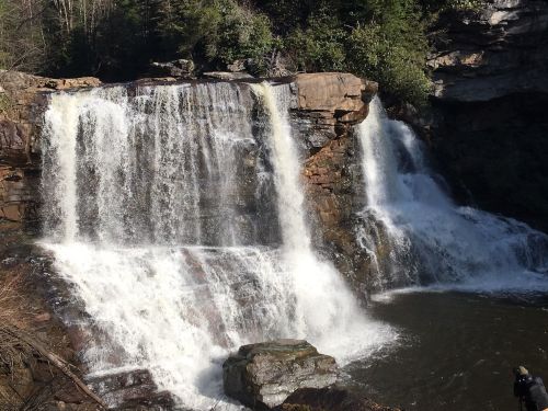 A scenic waterfall cascading over rocky cliffs into a serene pool, surrounded by lush greenery.