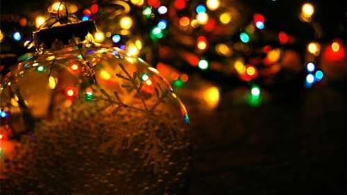 A close-up of a glass ornament with a snowflake inside, surrounded by colorful Christmas lights.