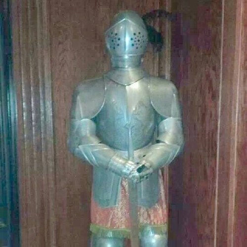 A full suit of medieval armor displayed on a wooden background, showcasing intricate metalwork and design.