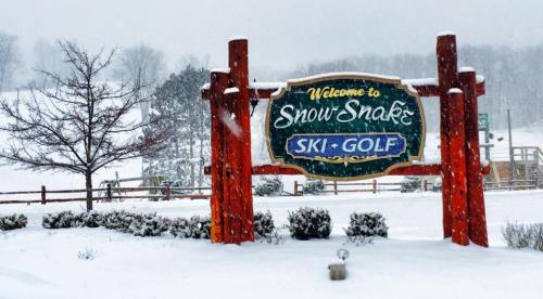 Sign for Snow Snake Ski-Golf surrounded by heavy snowfall and winter scenery.