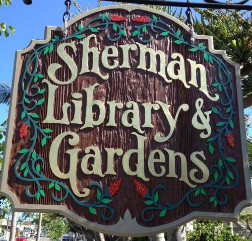 Sign for Sherman Library & Gardens, featuring decorative lettering and floral accents against a wooden background.