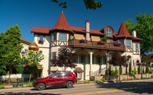 A charming, multi-story house with a turret and decorative features, surrounded by trees and a red SUV parked in front.