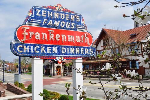 Colorful sign for Zehnder's Famous Frankenmuth Chicken Dinners, with a charming building and blooming flowers in the background.