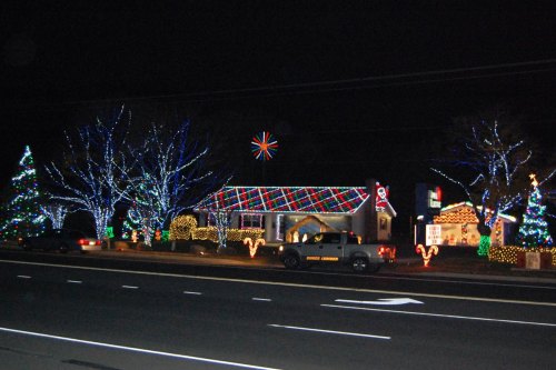 A festive display of colorful Christmas lights on houses and trees along a dark street at night.