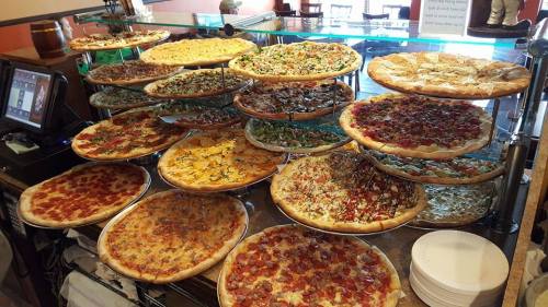A display of various pizzas on stacked trays, featuring different toppings and crust styles in a restaurant setting.