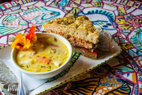 A bowl of creamy soup beside a sandwich on a colorful patterned table, garnished with edible flowers.