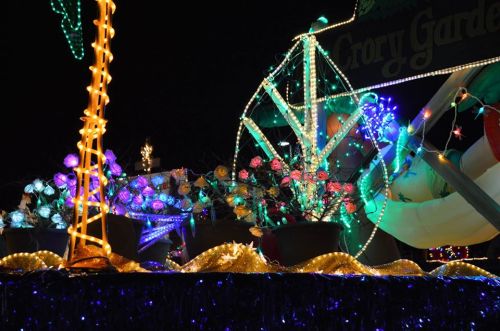 A colorful float adorned with bright lights, flowers, and festive decorations, set against a dark night sky.