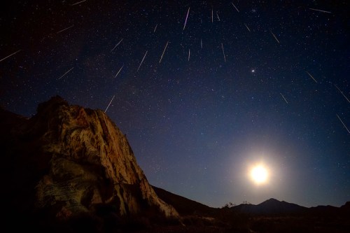 A night sky filled with shooting stars above a rocky landscape, illuminated by a bright moon.