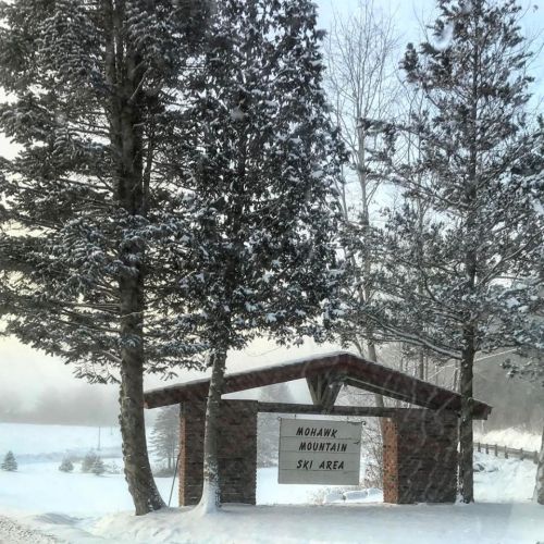 Sign for Mohawk Mountain Ski Area surrounded by tall trees in a snowy landscape.