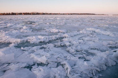 A frozen lake with large ice chunks scattered across the surface, under a soft pastel sky at dusk.