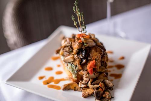 A gourmet dish featuring layered mushrooms, herbs, and vegetables on a white plate, garnished with a sprig of thyme.