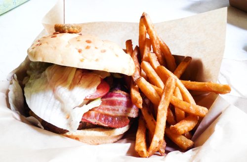 A juicy burger with bacon, lettuce, and a crispy onion ring, served with a side of golden French fries.