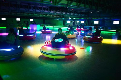 A vibrant indoor bumper car arena with colorful lights and people enjoying rides on illuminated bumper cars.