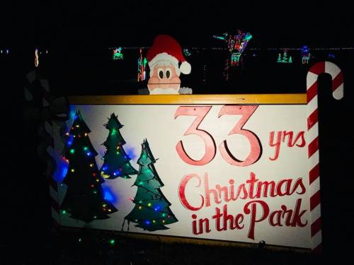 A festive sign reading "33 yrs Christmas in the Park" with a Santa figure and decorated trees, illuminated at night.