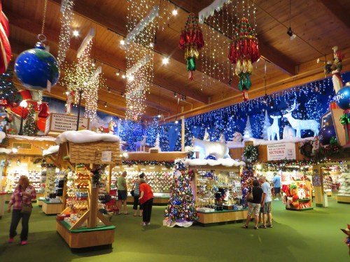 A festive store filled with Christmas decorations, lights, and trees, with shoppers browsing among colorful displays.