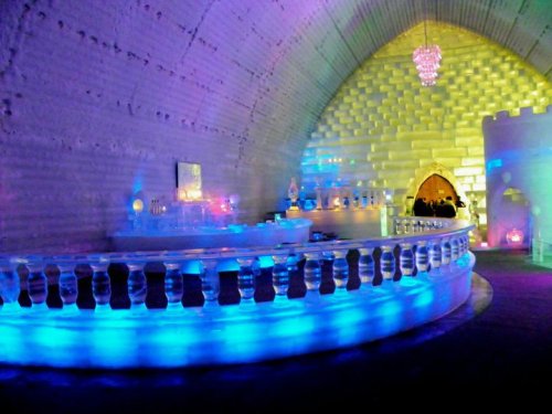 A colorful ice bar with illuminated walls and a curved counter, featuring a chandelier and a cozy atmosphere.