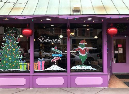 Colorful holiday window display featuring a Christmas tree, gifts, and a festive character in a purple storefront.
