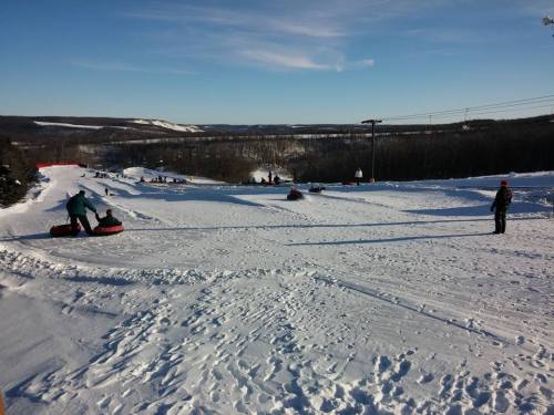 A snowy hill with people tubing and enjoying winter activities under a clear blue sky.