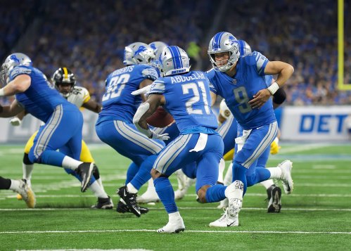 A Detroit Lions player runs with the ball while teammates block during a football game against the Pittsburgh Steelers.