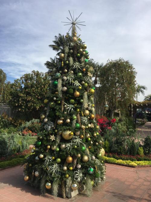 A beautifully decorated Christmas tree with green and gold ornaments, set in a lush garden.