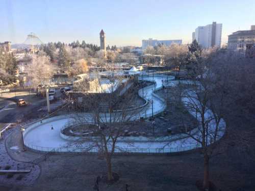 A winter scene of a frozen park with a winding path, trees, and a clock tower in the background.