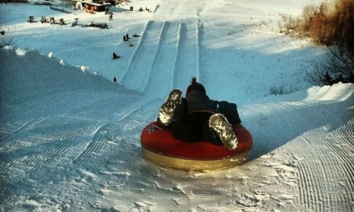 A person on a snow tube prepares to slide down a snowy hill, with other tubers in the background.