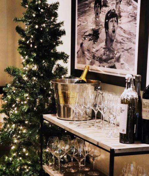 A festive scene featuring a Christmas tree, champagne, wine bottles, and elegant glasses on a shelf.