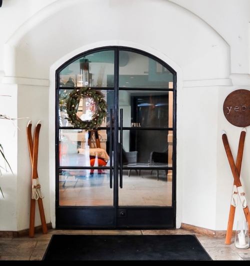 A glass door with a wreath, flanked by vintage skis, leading into a stylish interior space.